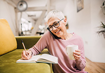 Vrouw schrijft met telefoon tussen schouder en oor